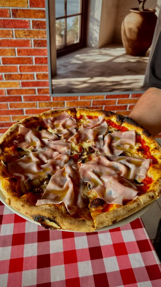 Pizza Capricciosa trzymana przez pizzaiola